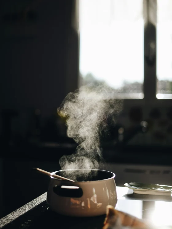 Pentolino da cucina con vapore su piano cottura, in una cucina illuminata dalla luce naturale.
